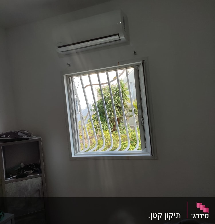 מזגן מותקן על קיר מעל חלון עם סורגים